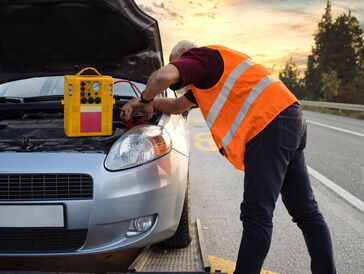 A roadside technician jump-starting a car stranded on the road. 