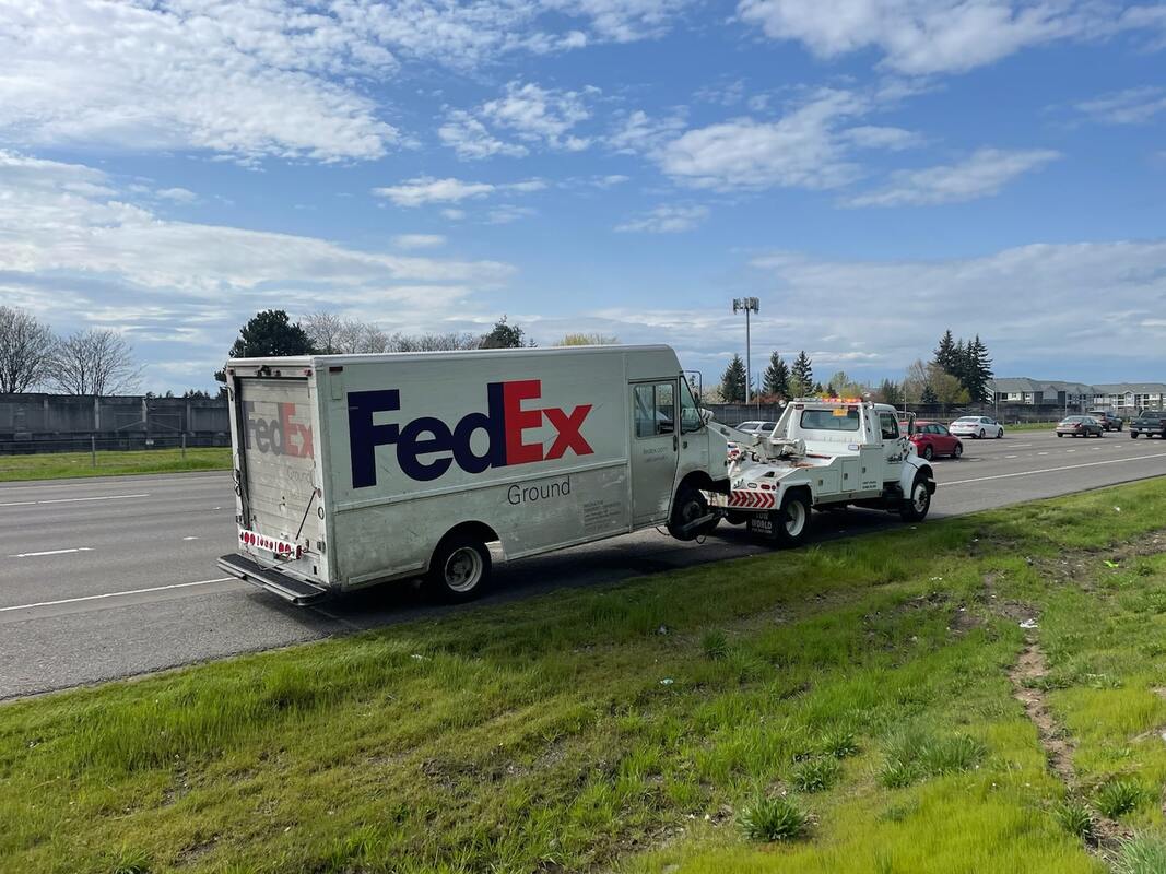 A tow truck towing a broken down FedEx truck.